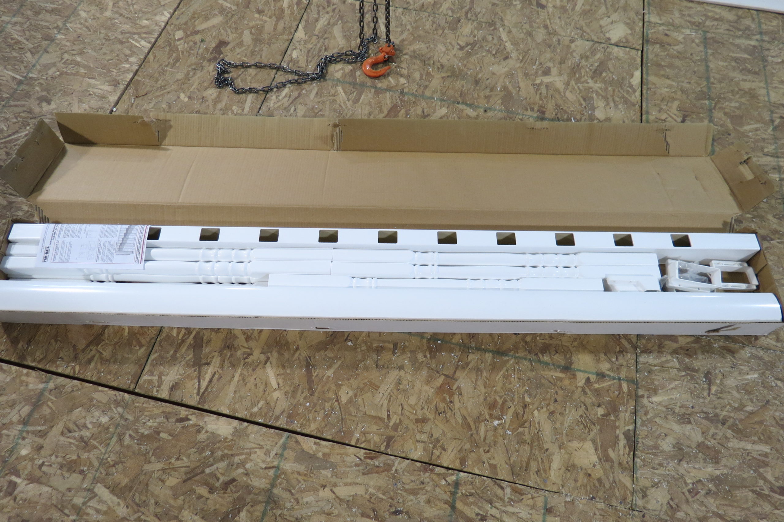 White vinyl railing kit components including rails and baluster connectors laid out in a cardboard shipping box
