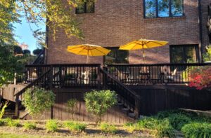 Large raised deck with black aluminum railing, stairs, and yellow patio umbrellas at brick home