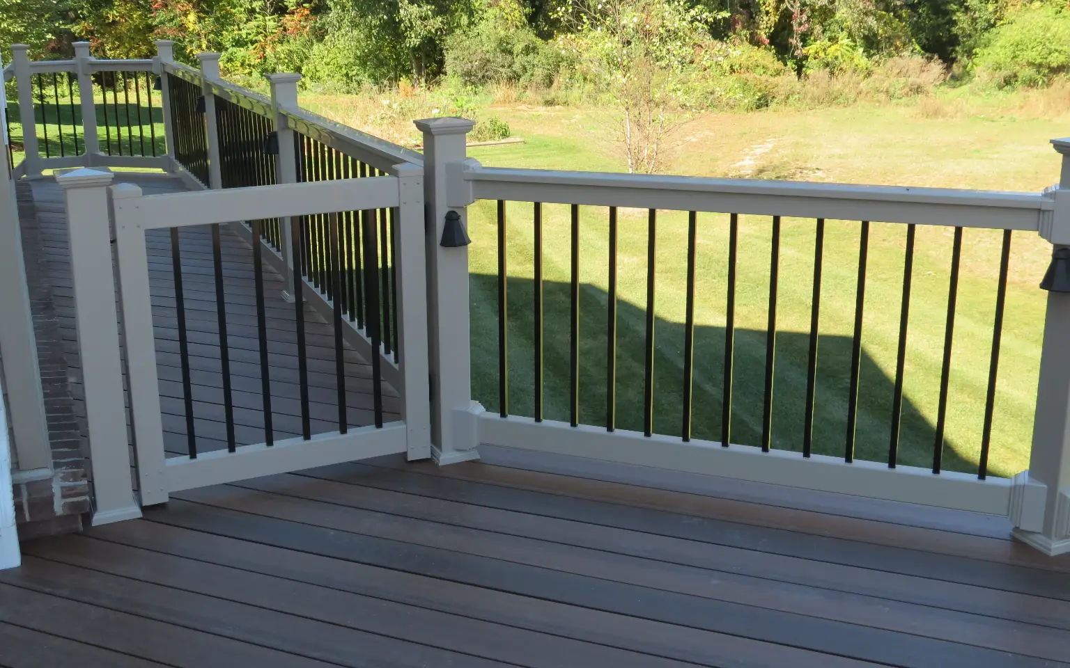 Composite deck with white vinyl railing gate and black aluminum balusters overlooking a shaded green yard