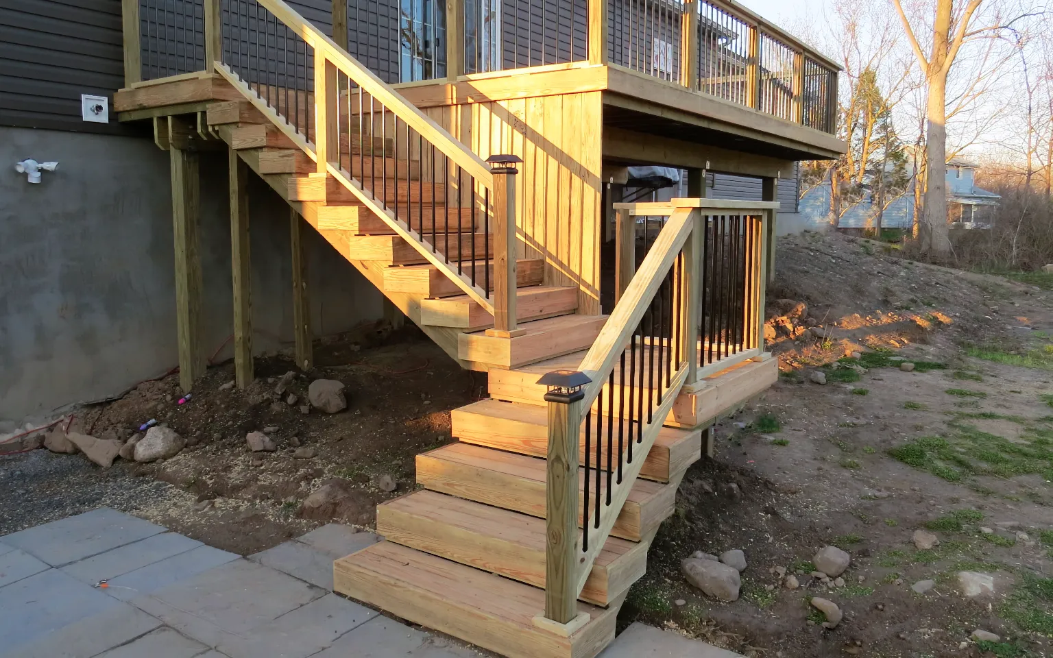 Raised pressure-treated wood deck with black aluminum balusters wood railing and stairs leading to a paver patio